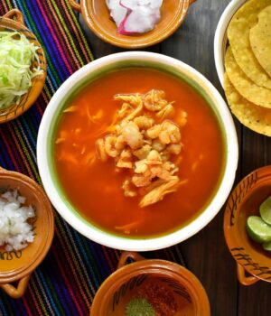 Top view of a traditional pozole soup with various fresh garnishes, perfect for authentic Mexican cuisine enthusiasts.