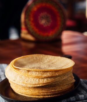 A stack of freshly made corn tortillas on a plate in a cozy, rustic setting with warm lighting.