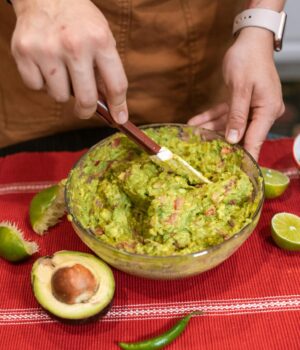 Close-up of hands mixing homemade guacamole with fresh ingredients in a kitchen setting.